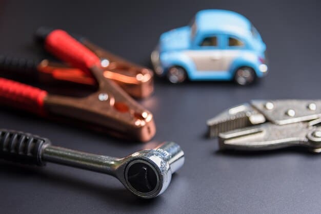 A photograph displaying a collection of tools typically used for car battery maintenance. The tools include a wire brush, battery terminal cleaner, wrench set, voltmeter, safety gloves, and safety glasses, arranged neatly on a workbench.