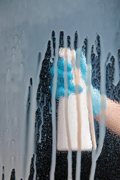 Close-up of a hand using a microfiber wash mitt to gently wash the side of a car. The two-bucket system is visible nearby, with one bucket filled with soapy water and the other with clean rinse water.