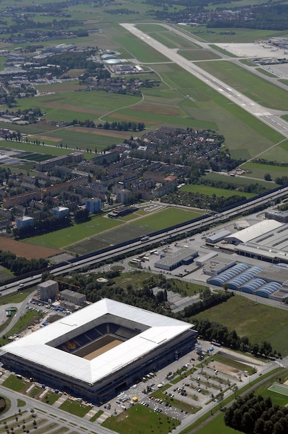 An aerial view of a large automobile manufacturing plant in the US, with solar panels covering the roof and electric vehicle charging stations in the parking lot. Green landscaping surrounds the facility, showcasing the manufacturer's commitment to sustainability. The image is taken on a sunny day with clear visibility.