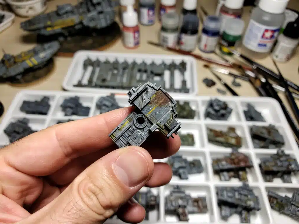 Hand holding intricately painted scale model component with weathering effects.